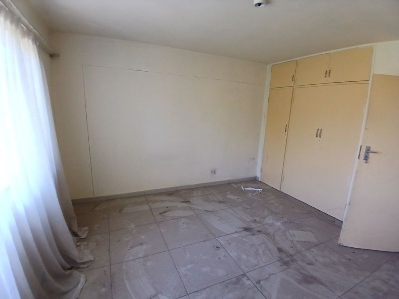 An empty bedroom featuring tiled flooring, built-in cupboards, and a curtain rail, requiring cosmetic updates to improve its overall condition.