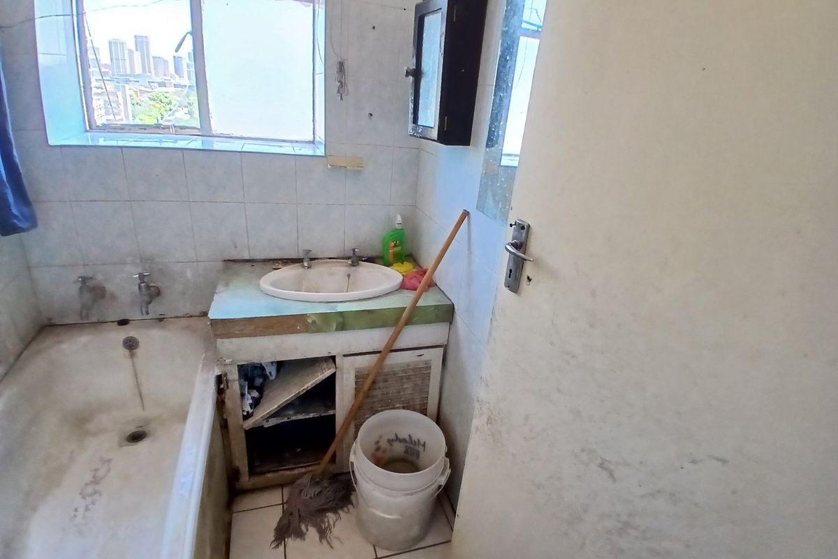 A dated bathroom featuring a built-in vanity, ceramic basin, and bathtub, requiring significant renovation and modernization of fixed finishes.