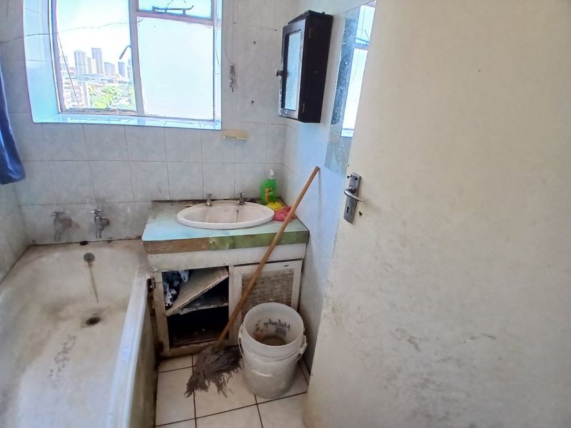 A dated bathroom featuring a built-in vanity, ceramic basin, and bathtub, requiring significant renovation and modernization of fixed finishes.