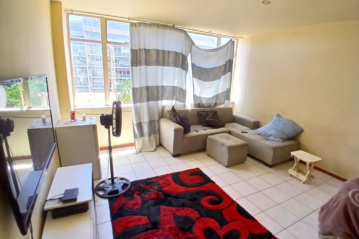 A living room featuring tiled flooring and a large window, providing natural light. The space is ready for a modern update to enhance its appeal.