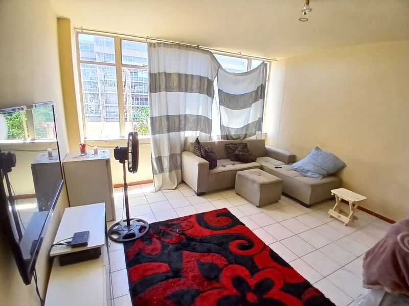 A living room featuring tiled flooring and a large window, providing natural light. The space is ready for a modern update to enhance its appeal.