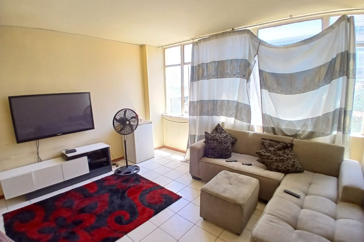 A living room featuring tiled flooring and large windows that provide natural light, offering a blank canvas for potential interior updates.