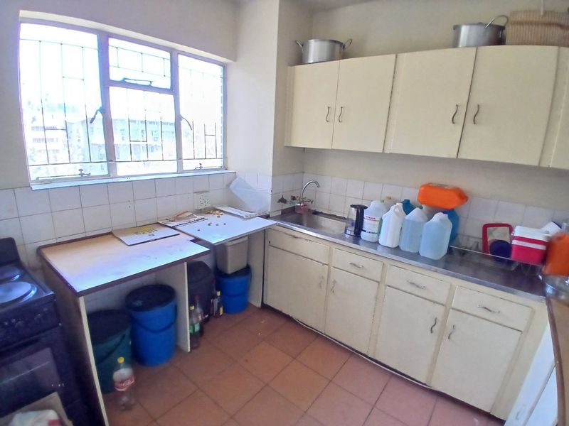 A functional kitchen featuring built-in cabinetry, a stainless steel sink, tiled backsplash, and tiled flooring, offering potential for modernization and renovation.