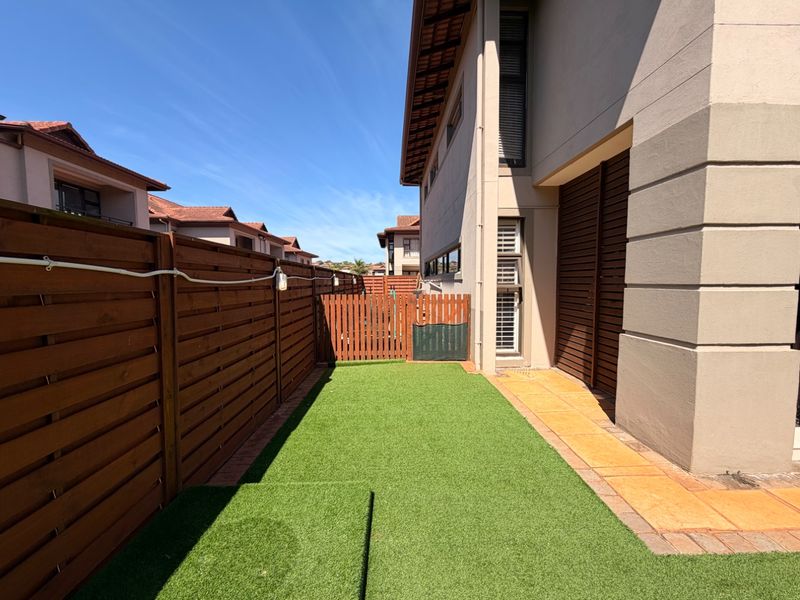 A well-maintained rear courtyard featuring artificial turf, timber boundary fencing, a paved walkway, and secure gated access.
