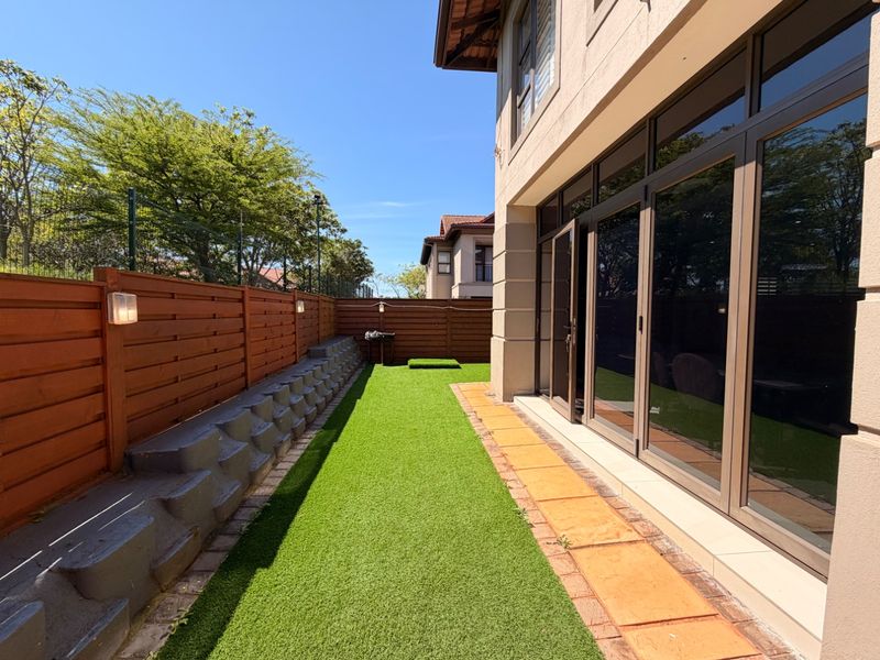 A well-maintained rear garden featuring artificial turf, a paved walkway, timber fencing, and large aluminium-framed glass doors leading into the townhouse.