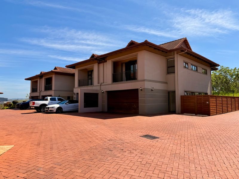 Front elevation of a multi-story townhouse complex featuring a paved driveway, integrated garage, and upper-level balconies.