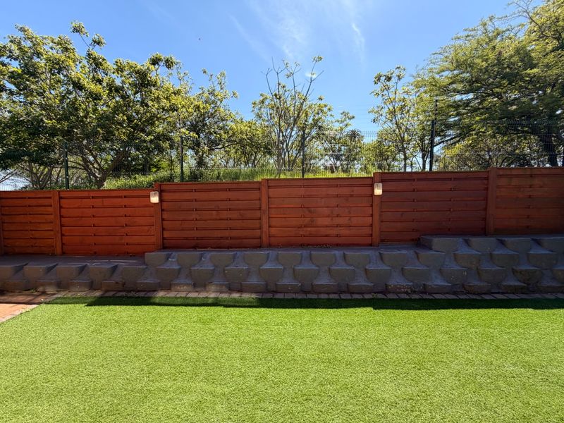 A well-maintained garden area featuring artificial turf, a tiered concrete retaining wall, and a modern timber slat boundary fence.