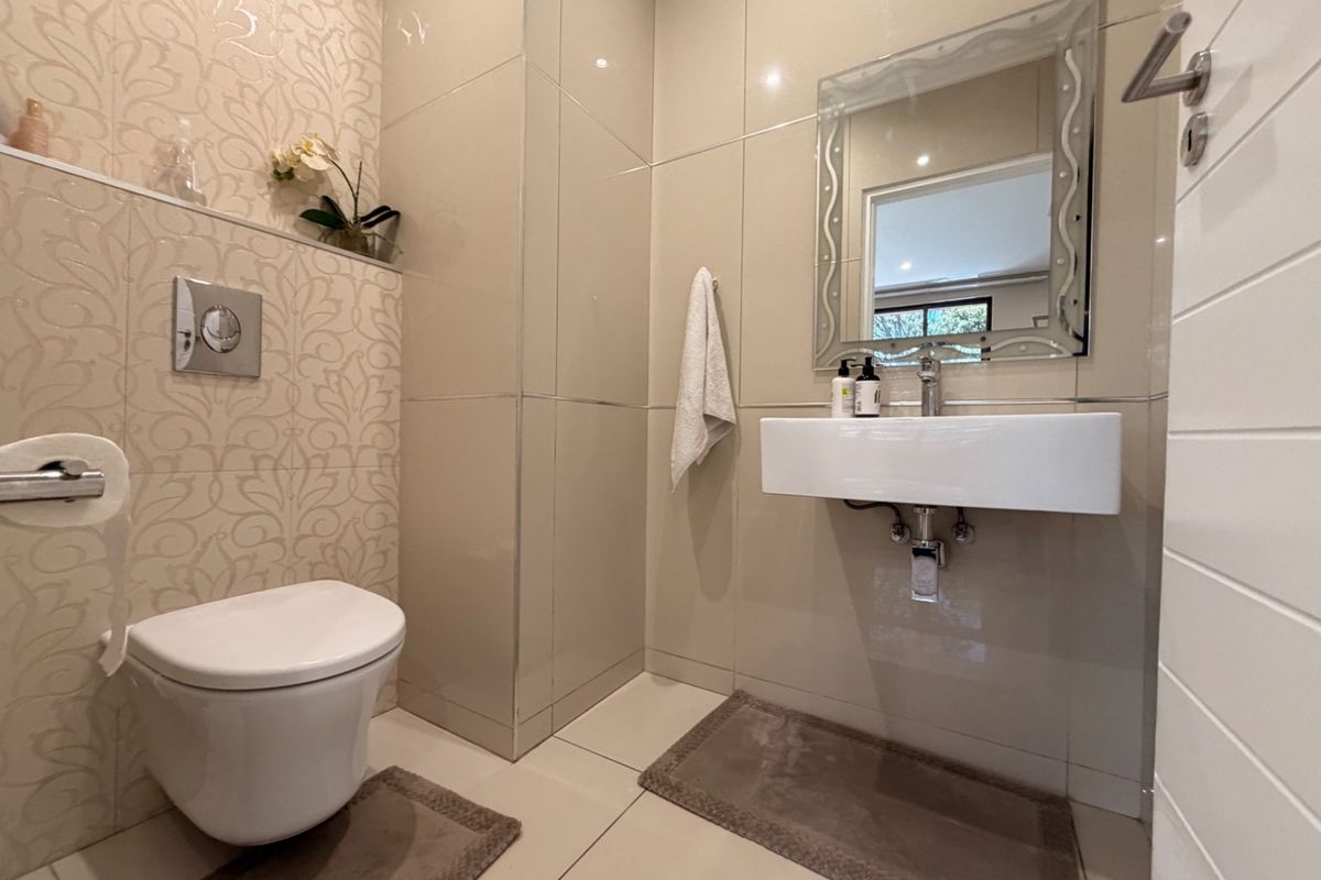 A modern guest bathroom featuring a wall-mounted toilet, sleek wall-mounted basin, and neutral floor-to-ceiling tiling with decorative accent wall detail.