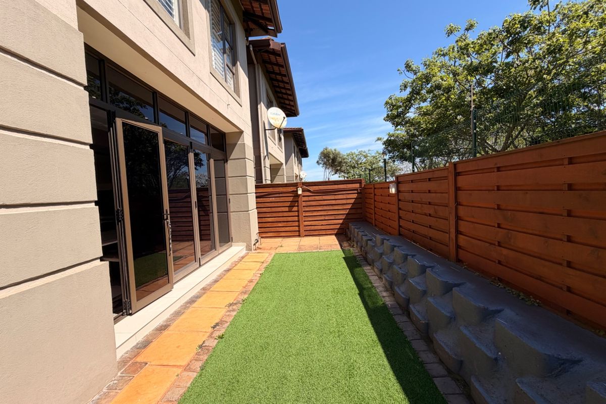 A well-maintained rear garden area featuring artificial turf, a timber fence, a retaining wall, and bi-fold doors leading into the townhouse.