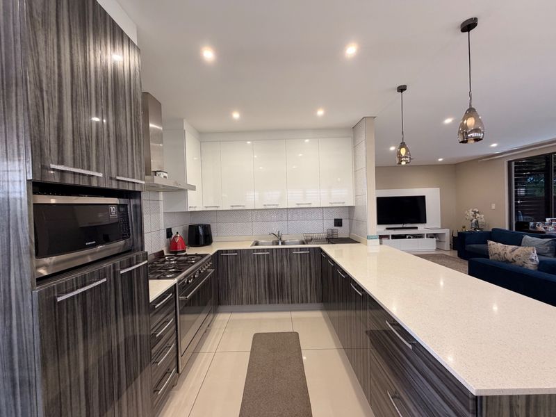 Modern open-plan kitchen featuring high-gloss cabinetry, quartz countertops, integrated appliances, and a breakfast bar, seamlessly flowing into the adjacent living area.