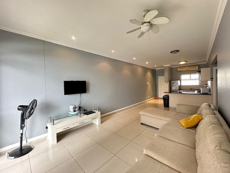 Open-plan living area featuring tiled floors, recessed lighting, a ceiling fan, and a functional kitchen with a breakfast bar and cabinetry.