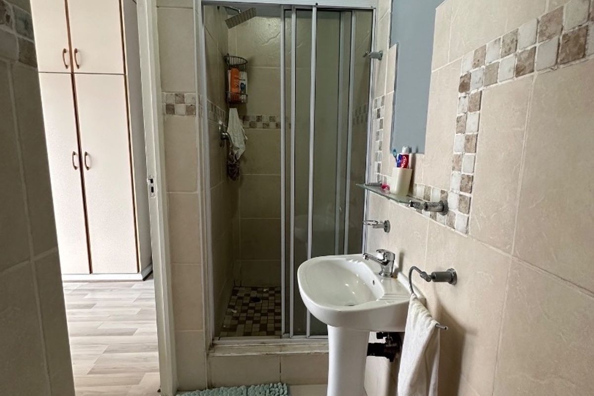 A functional bathroom featuring a pedestal basin, tiled walls, and a separate shower enclosure with a glass door.