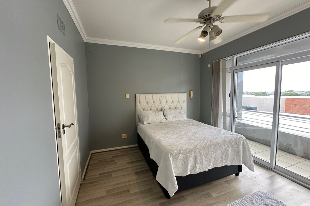 A well-lit bedroom featuring laminate flooring, crown molding, a ceiling fan, and direct access to a private balcony through sliding glass doors.