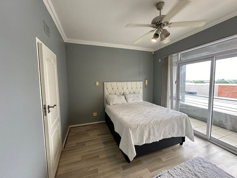 A well-lit bedroom featuring laminate flooring, crown molding, a ceiling fan, and direct access to a private balcony through sliding glass doors.