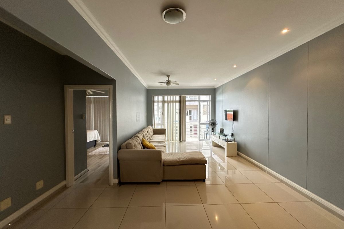 Spacious living room featuring large format floor tiles, neutral wall tones, recessed lighting, and a ceiling fan, with direct access to a balcony.