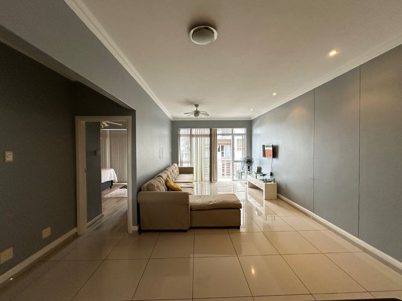 Spacious living room featuring large format floor tiles, neutral wall tones, recessed lighting, and a ceiling fan, with direct access to a balcony.
