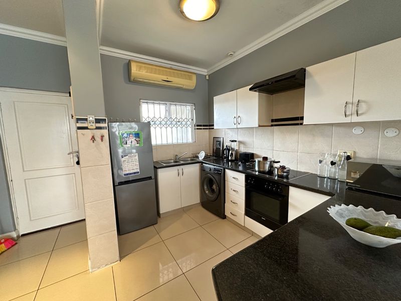 Functional kitchen featuring granite countertops, built-in cabinetry, electric oven with hob, extractor fan, and tiled flooring with a neutral color scheme.