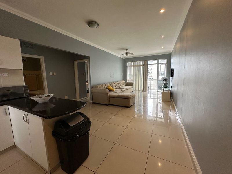 Spacious open-plan living area featuring tiled floors, recessed lighting, and a modern kitchen with granite countertops, leading to a balcony with natural light.