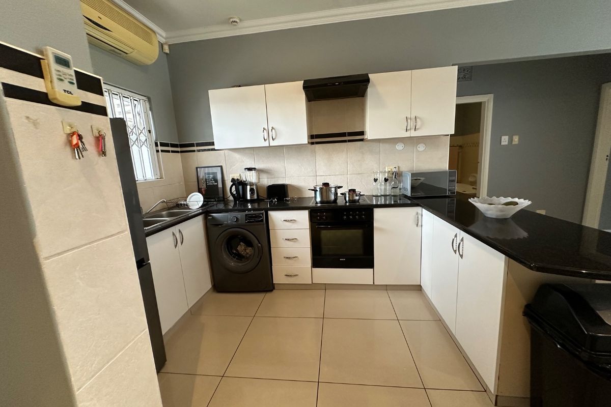 Functional kitchen featuring white cabinetry, granite countertops, built-in oven, hob, extractor fan, and tiled flooring with a breakfast bar area.
