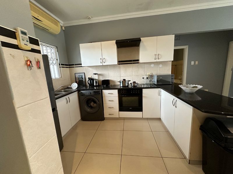 Functional kitchen featuring white cabinetry, granite countertops, built-in oven, hob, extractor fan, and tiled flooring with a breakfast bar area.