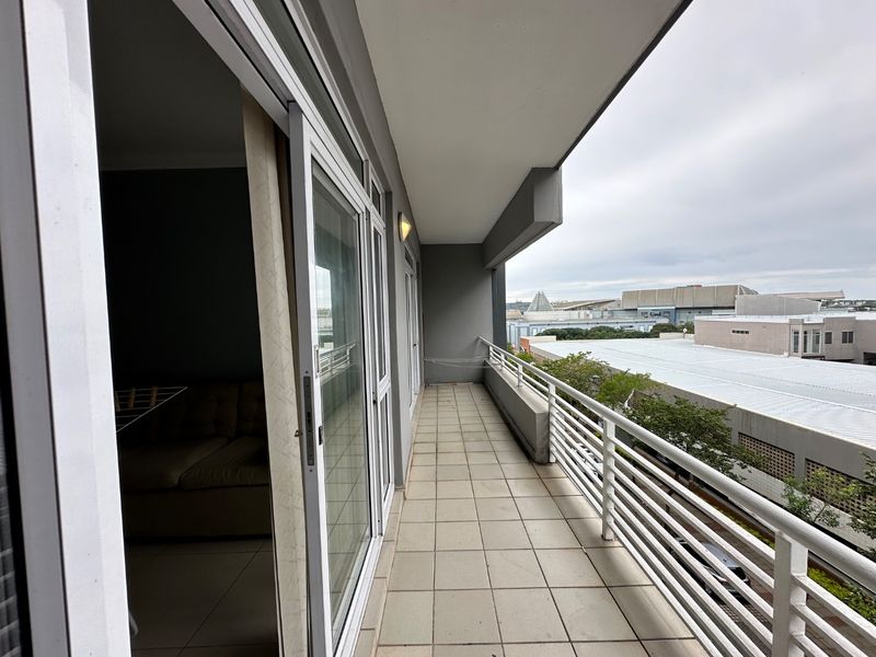 A spacious covered balcony featuring tiled flooring, a secure metal balustrade, and direct access to the interior through large sliding glass doors.