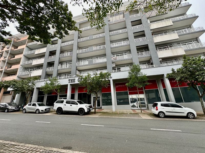 Street-level view of a multi-story apartment building featuring a modern facade with multiple balconies and ground-floor commercial storefronts.