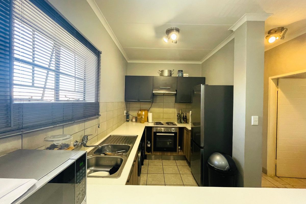 A functional kitchen featuring built-in cabinetry, a stainless steel sink, integrated oven and hob, tiled flooring, and a tiled backsplash.