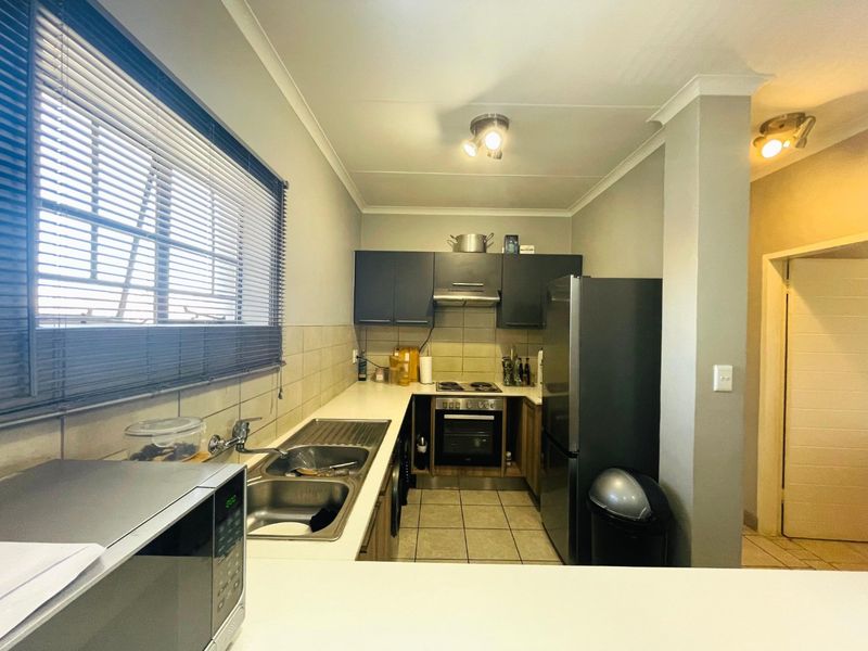 A functional kitchen featuring built-in cabinetry, a stainless steel sink, integrated oven and hob, tiled flooring, and a tiled backsplash.