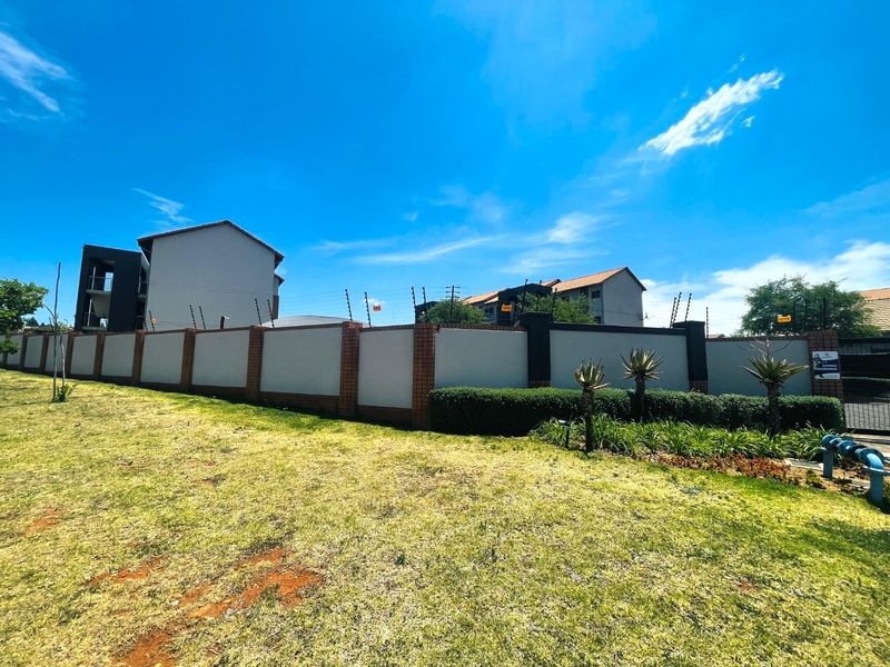 Exterior view of the apartment complex perimeter featuring a secure boundary wall with electric fencing and well-maintained landscaped grounds.