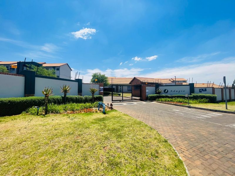 The entrance to the Adagio apartment complex features a secure gated access point, paved driveway, and well-maintained perimeter walls with electric fencing.