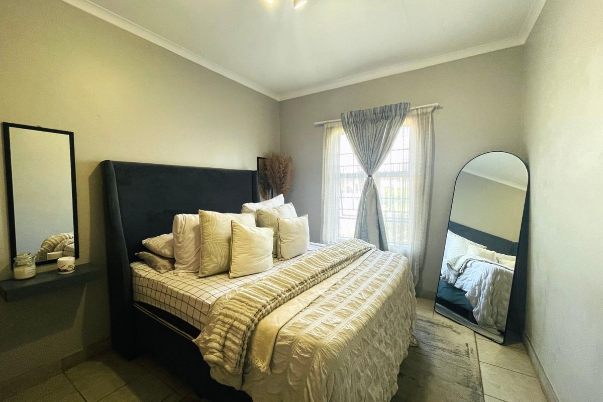 A well-maintained bedroom featuring tiled flooring, neutral wall finishes, and a window fitted with security bars.