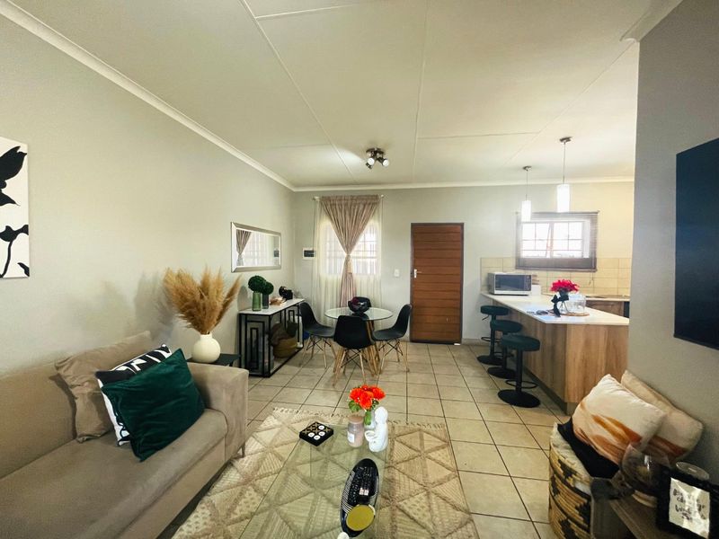 An open-plan living and kitchen area featuring tiled flooring, a functional kitchen island, and neutral wall finishes, creating a cohesive and practical living space.