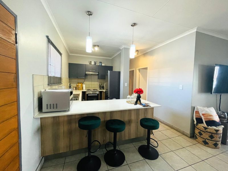 An open-plan kitchen featuring a breakfast bar, modern cabinetry, built-in appliances, and tiled flooring, seamlessly connecting to the living area.