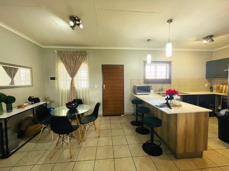 Open-plan kitchen and dining area featuring a breakfast bar island, tiled flooring, and modern pendant lighting, creating a functional and cohesive living space.