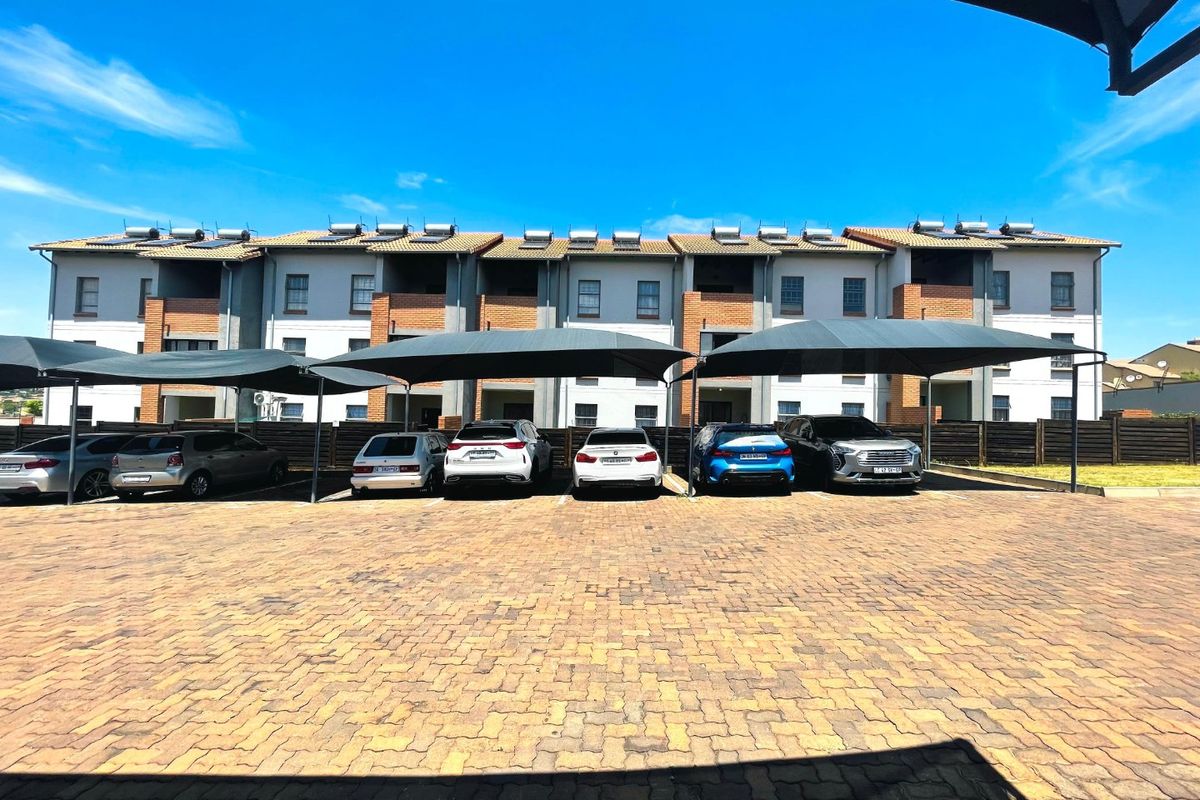 Exterior view of an apartment complex featuring a paved parking area with shade cloth carports and solar water heating units on the roof.