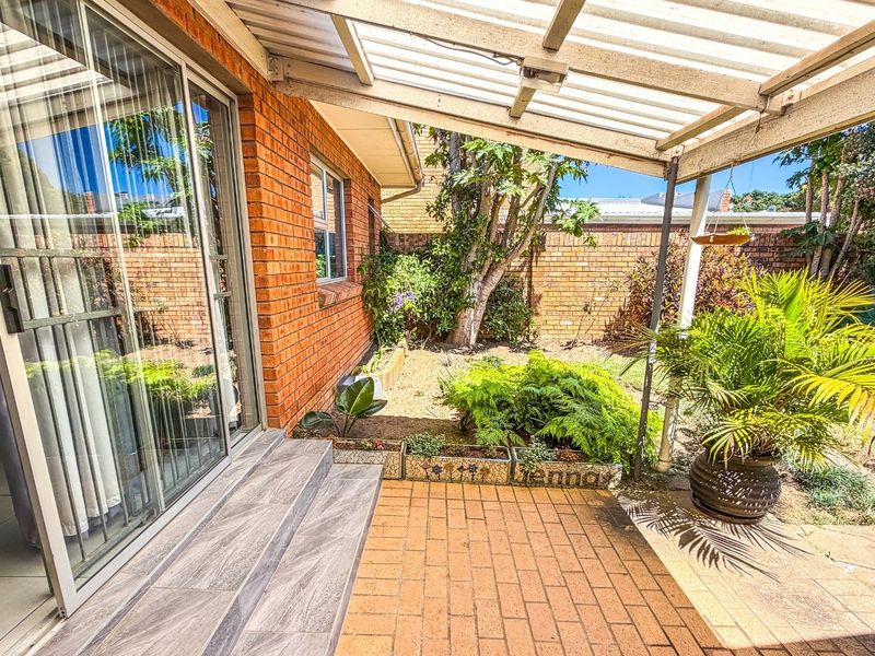 A covered brick-paved patio area featuring a translucent roof, providing a seamless transition from the interior living space to the private rear garden.