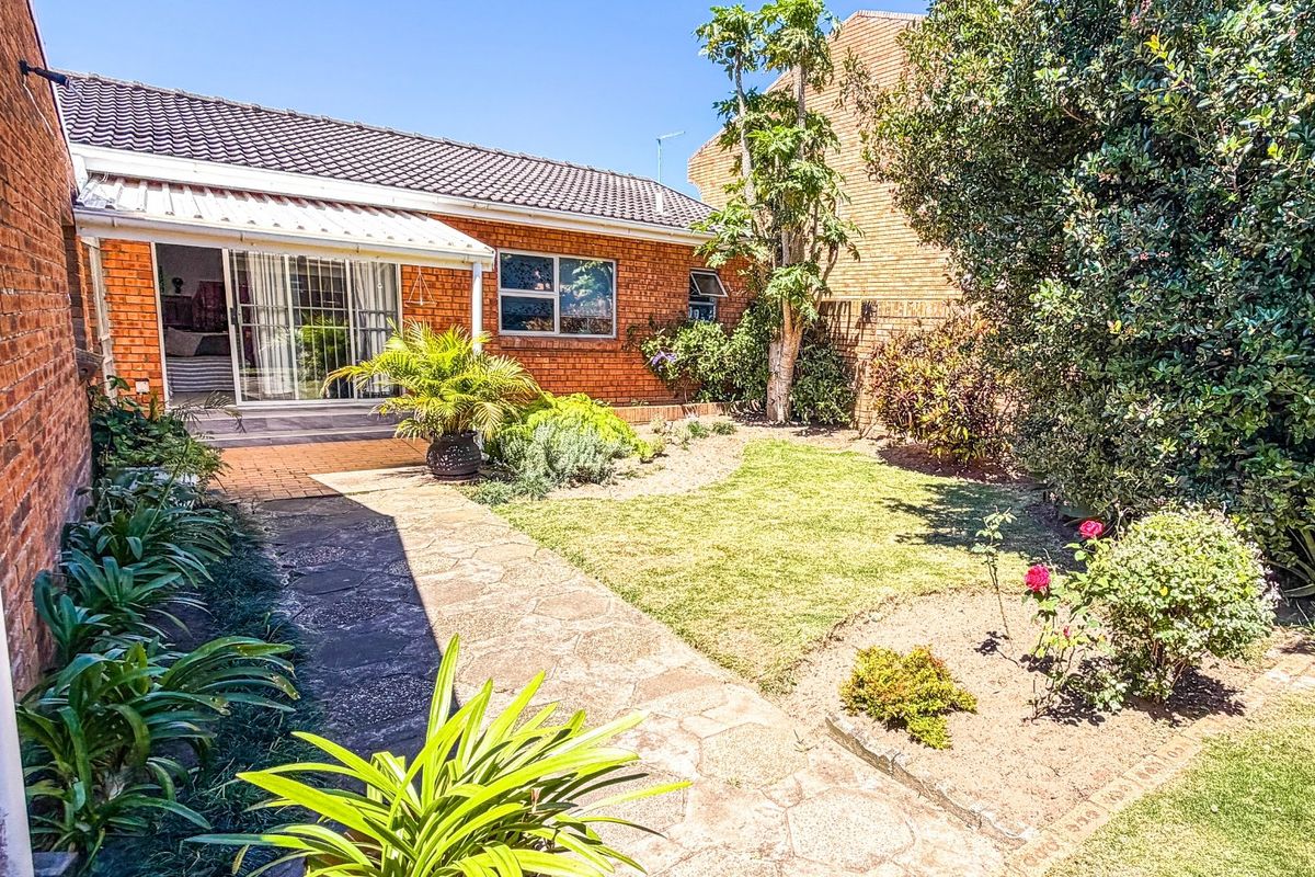 A private rear garden featuring a paved walkway, established landscaping, and a brick exterior with a sliding door leading to the interior living space.