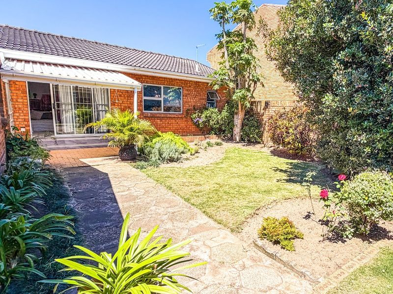 A private rear garden featuring a paved walkway, established landscaping, and a brick exterior with a sliding door leading to the interior living space.