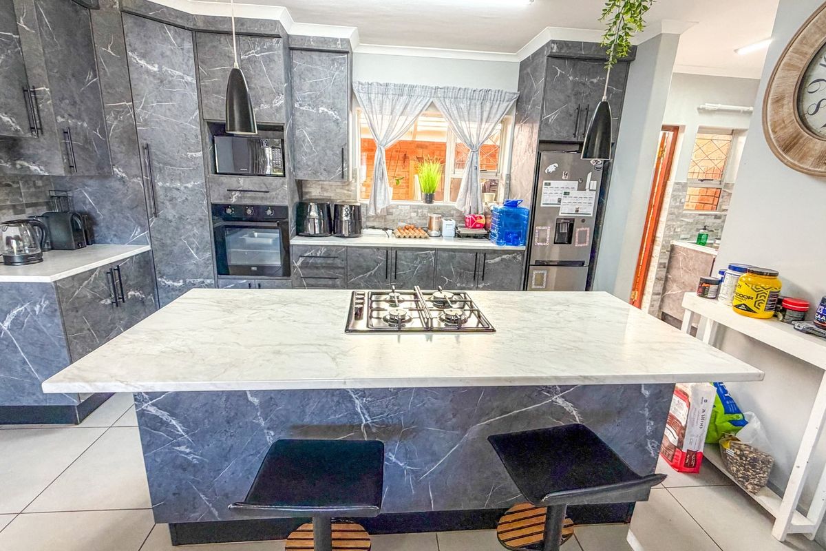 Modern kitchen featuring marble-effect cabinetry, a central island with a built-in gas hob, and integrated appliances, offering a sleek and functional cooking space.