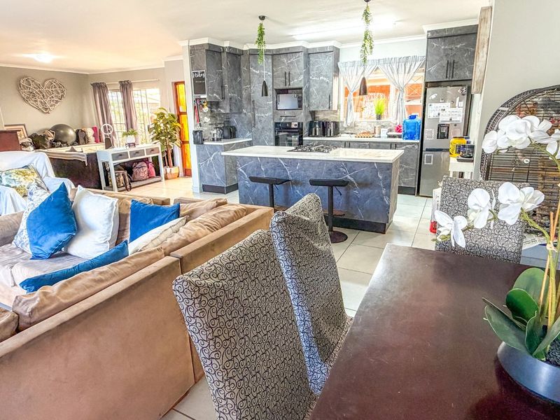 Open-plan living and kitchen area featuring marble-effect cabinetry, a central kitchen island with a hob, and tiled flooring throughout.