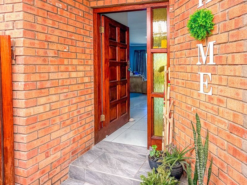 A welcoming entrance featuring an exposed brick facade, a solid timber panelled front door, and a tiled step leading into the home.