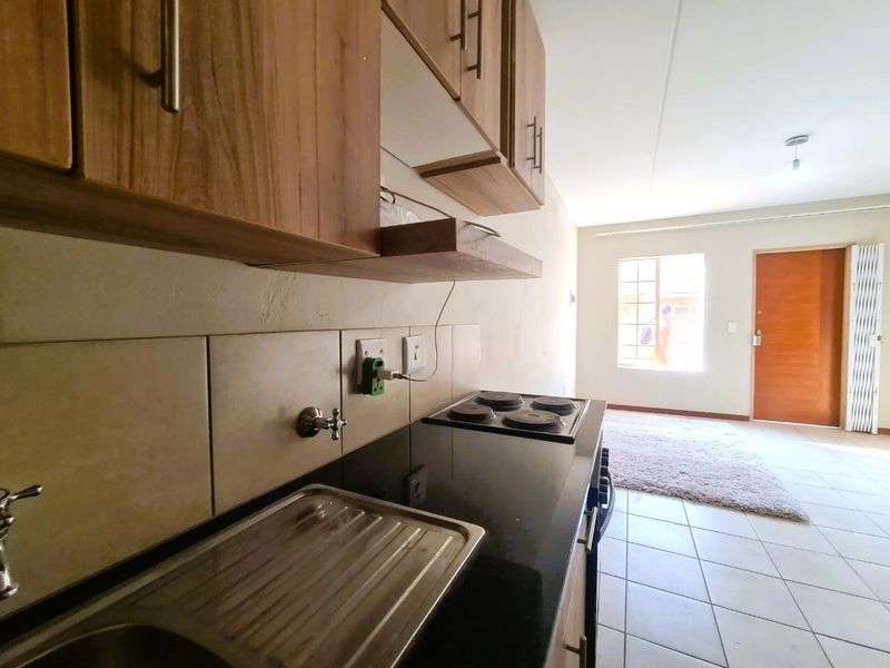 Open-plan kitchen and living area featuring built-in cabinetry, a stainless steel sink, electric hob, and tiled flooring throughout.