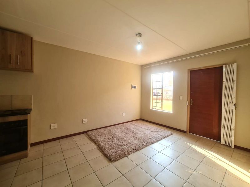 An open-plan living area featuring tiled flooring, a compact kitchen with built-in oven and hob, and direct access to the exterior via a security gate.