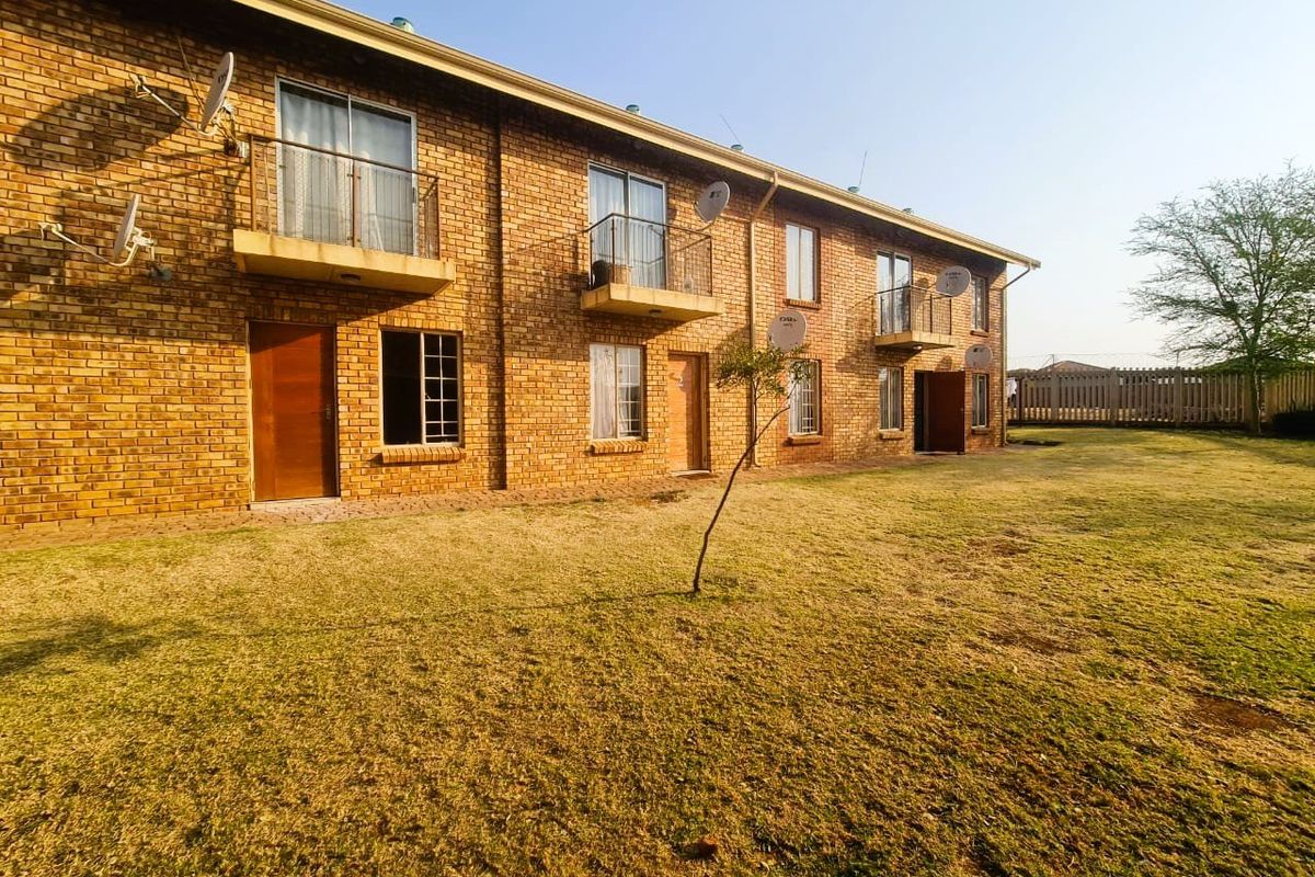 Rear view of a multi-story apartment complex featuring face brick construction, private balconies with metal railings, and access to a shared garden area.