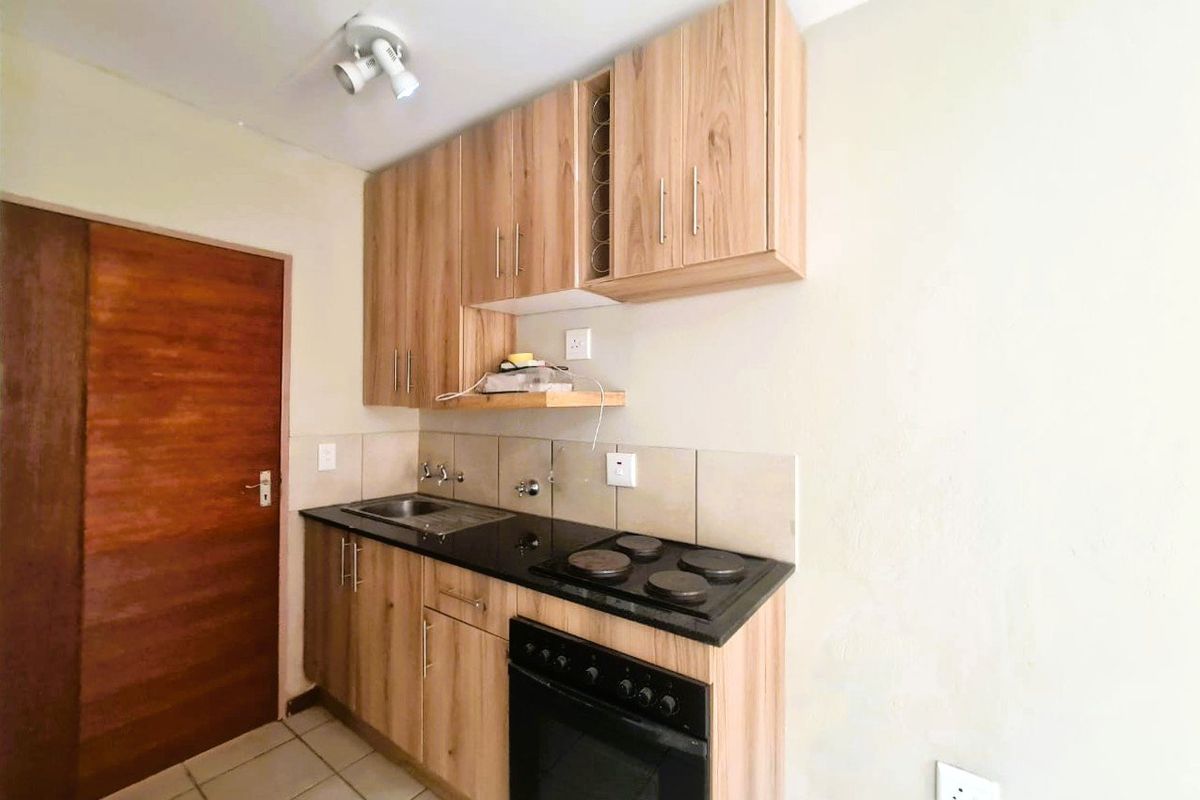 Compact kitchen featuring wood-look cabinetry, dark countertops, built-in oven and hob, tiled backsplash, and tiled flooring.