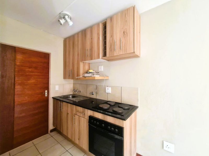 Compact kitchen featuring wood-look cabinetry, dark countertops, built-in oven and hob, tiled backsplash, and tiled flooring.