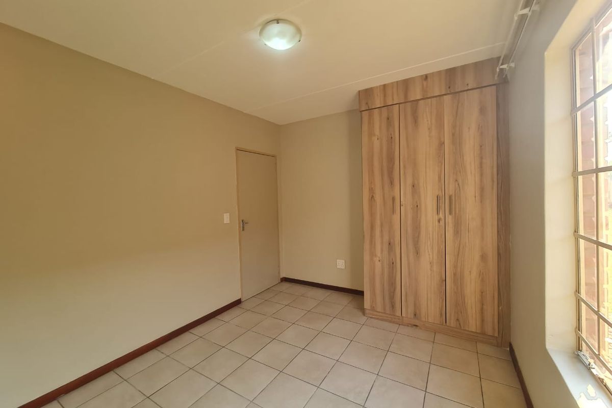 A clean, empty bedroom featuring neutral wall tones, tiled flooring, and modern wood-finish built-in cupboards with security bars on the window.