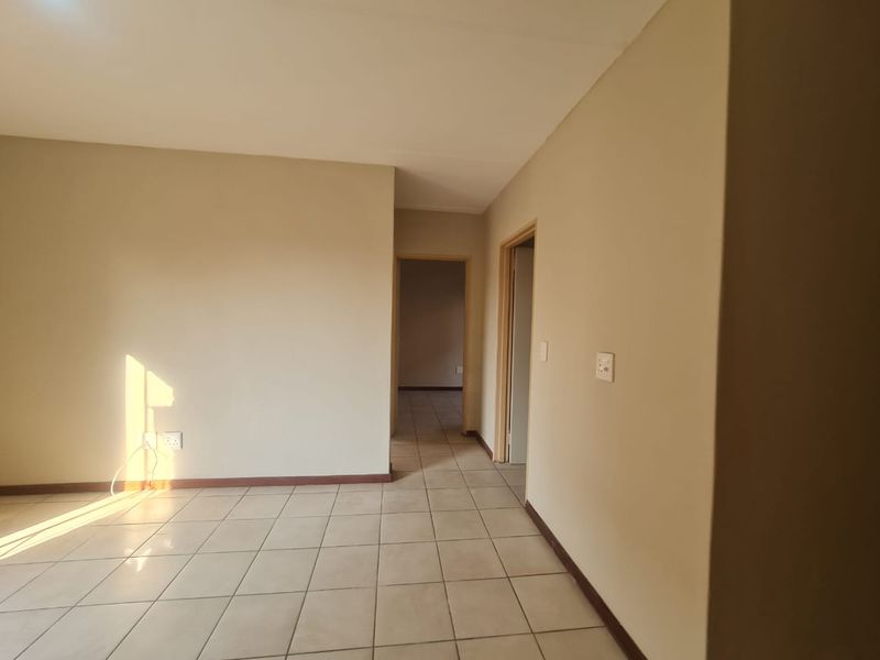 A bright, empty hallway featuring neutral wall paint and tiled flooring, providing access to adjacent rooms within the apartment.