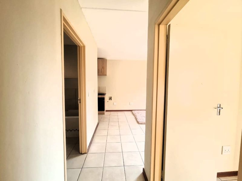 A view through a hallway leading into an open plan living area with tiled flooring and neutral wall finishes.