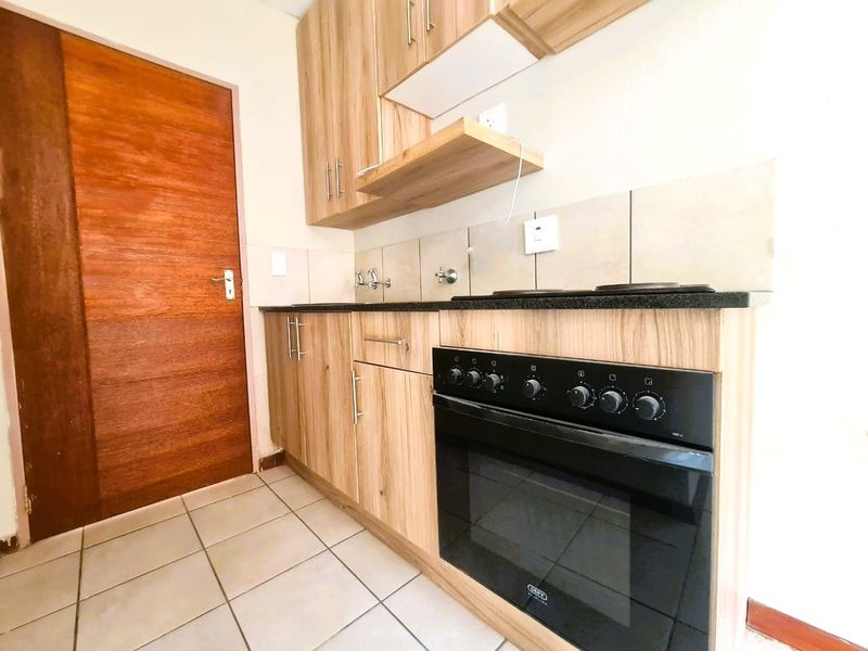 A compact kitchen featuring light wood-finish cabinetry, granite countertops, a built-in oven and hob, and tiled flooring.